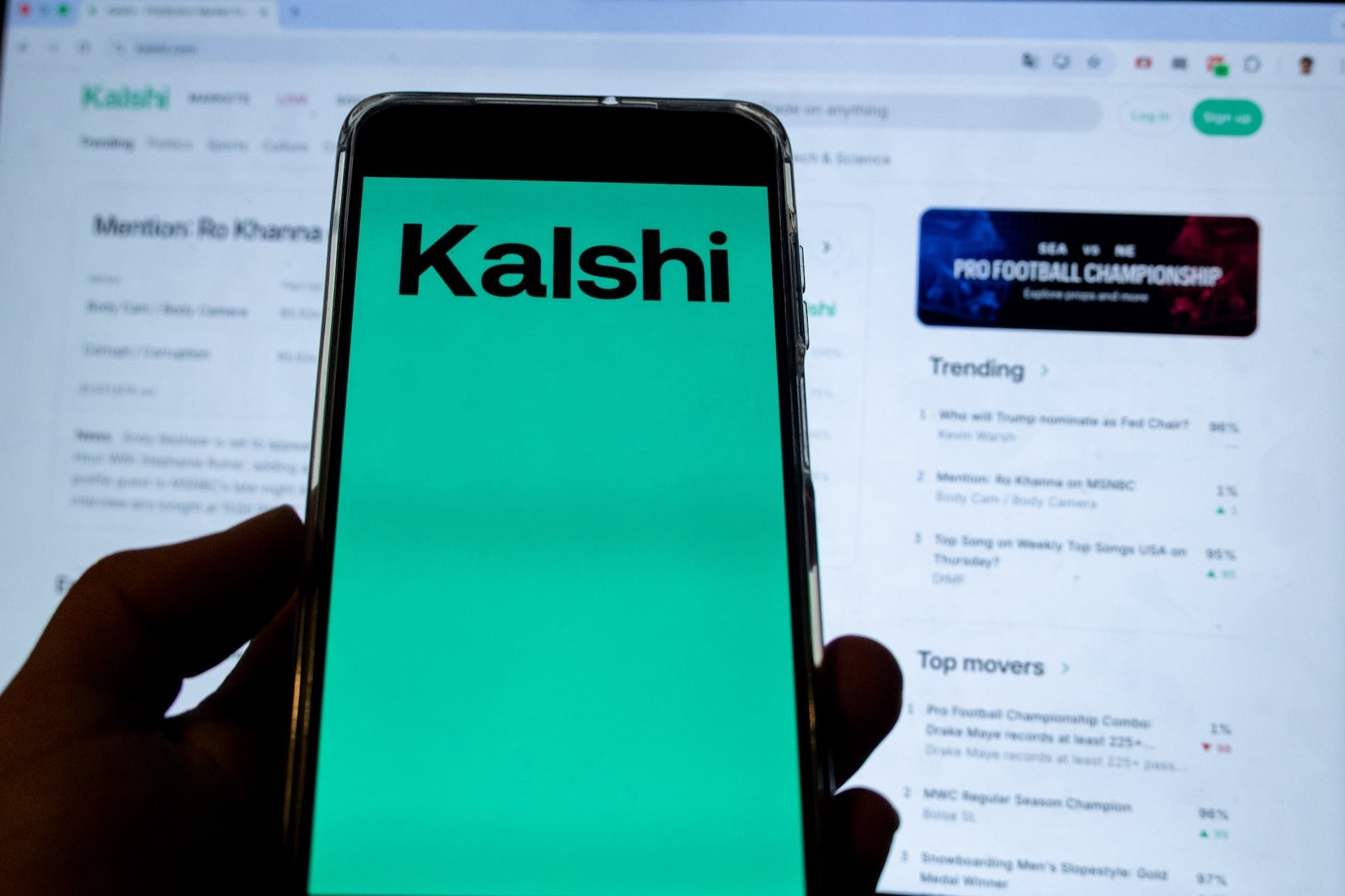 Smartphone screen shows Kalshi logo.