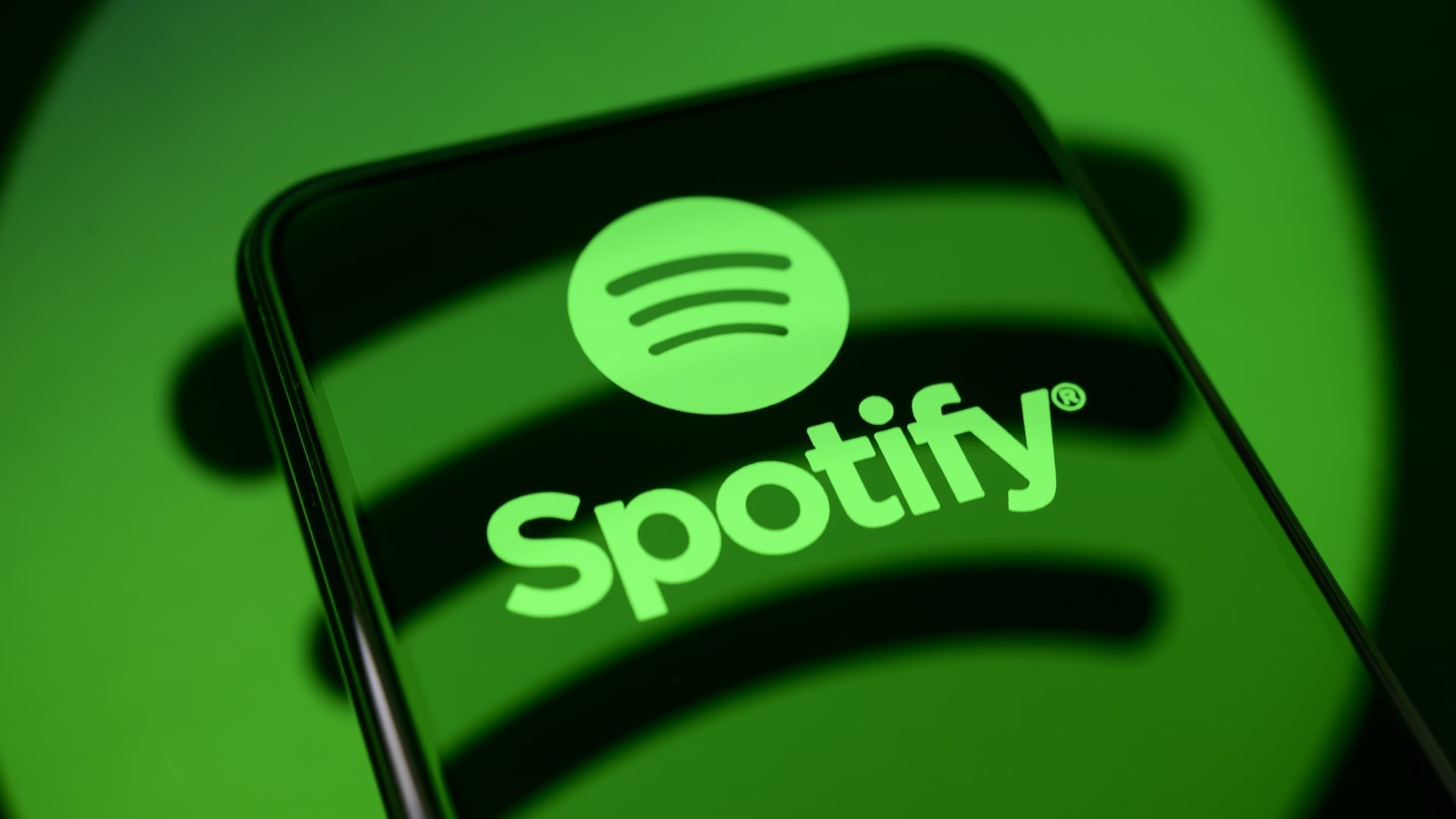 The Spotify logo is displayed on a smartphone screen placed on a reflective surface onto which the company's logo is projected,