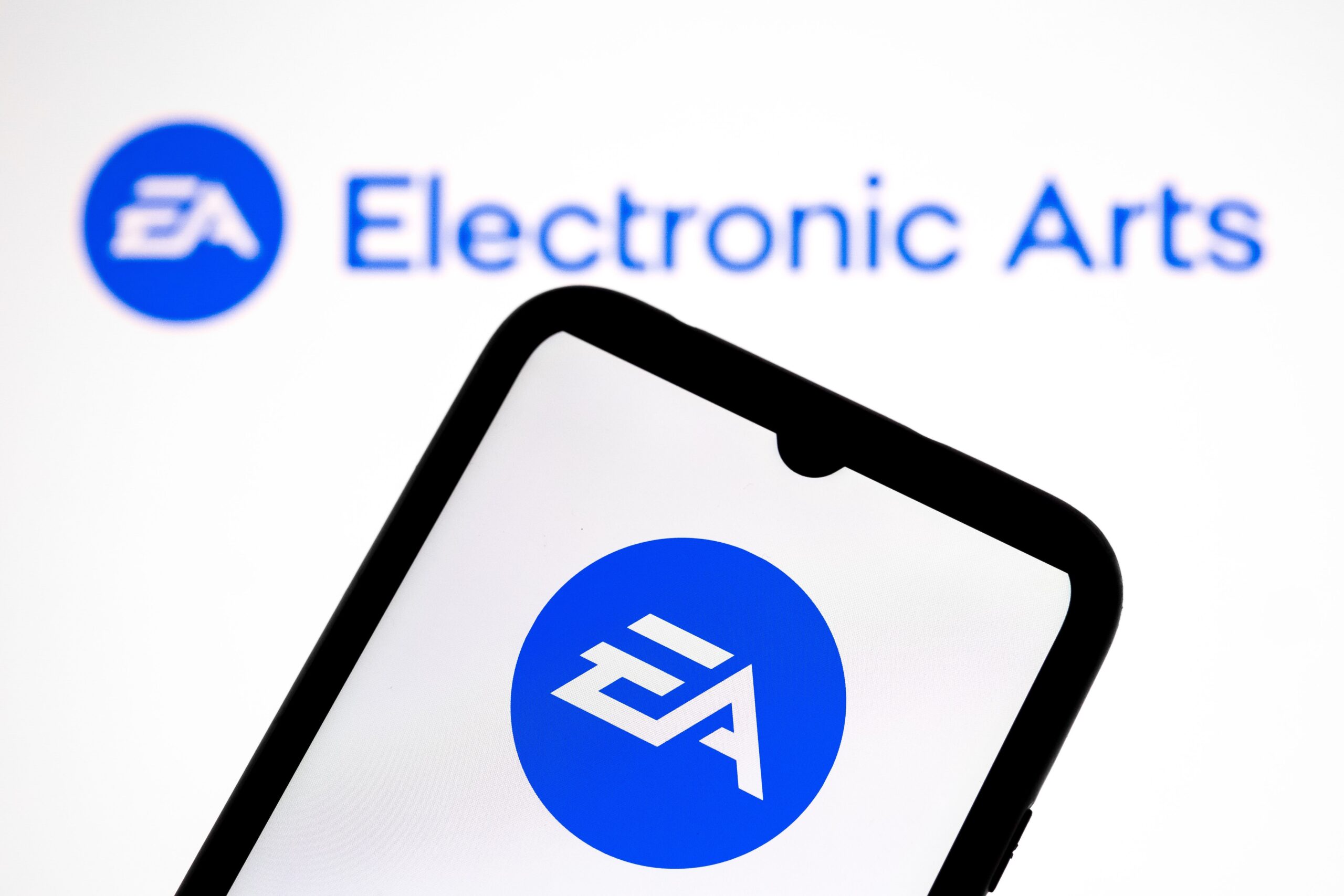 The Electronic Arts (EA) logo appears on a smartphone screen and as the background on a laptop computer screen in this photo illustration