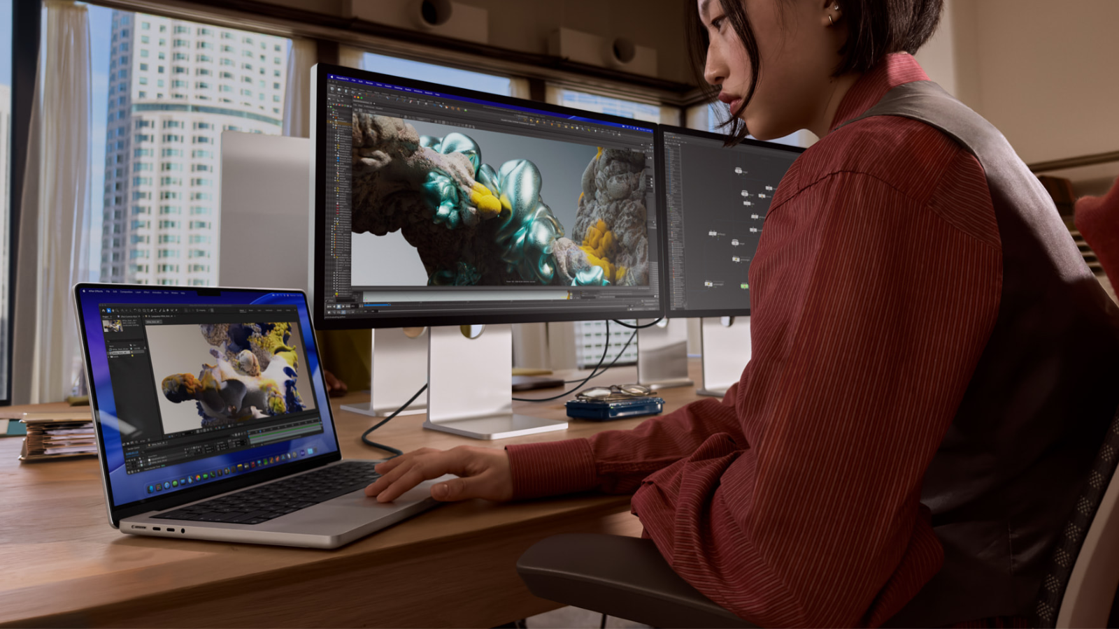a woman using a macbook pro that's connected to two external monitors