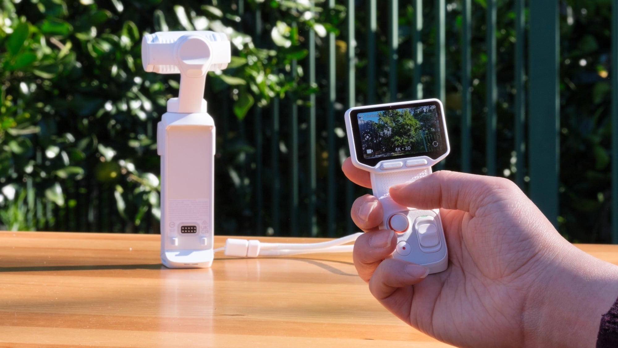 The Insta360 Luna Ultra set down in the background, with a hand holding its detached remotein the foreground.