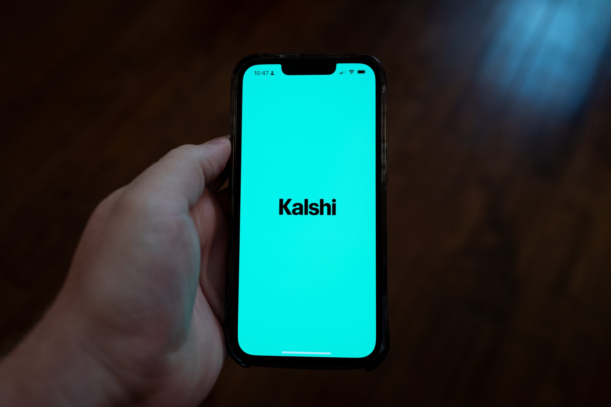 Close-up of a person's hand holding a smartphone displaying opening screen for the Kalshi app