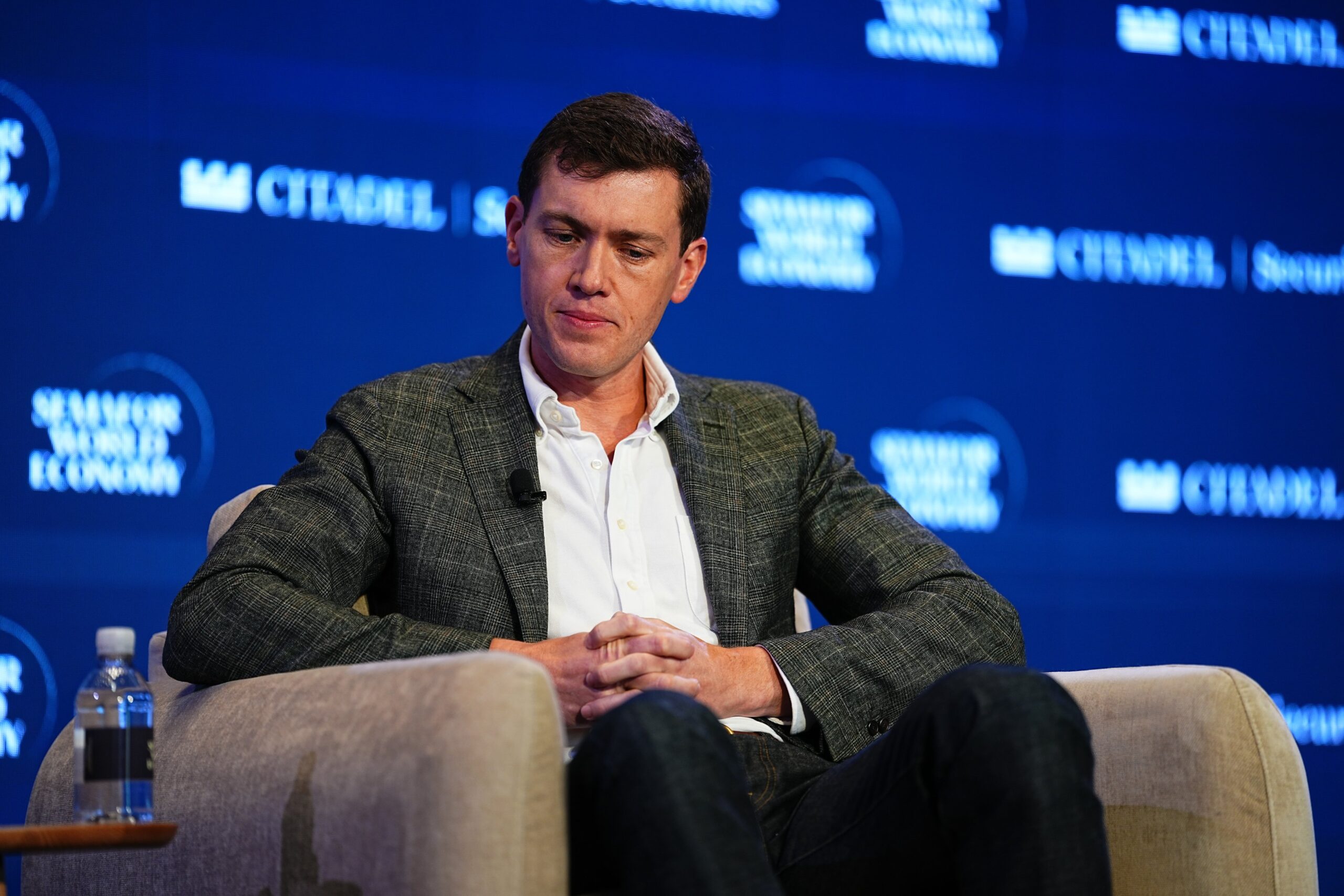 Garrett Langley sits in a chair on stage at a conference.