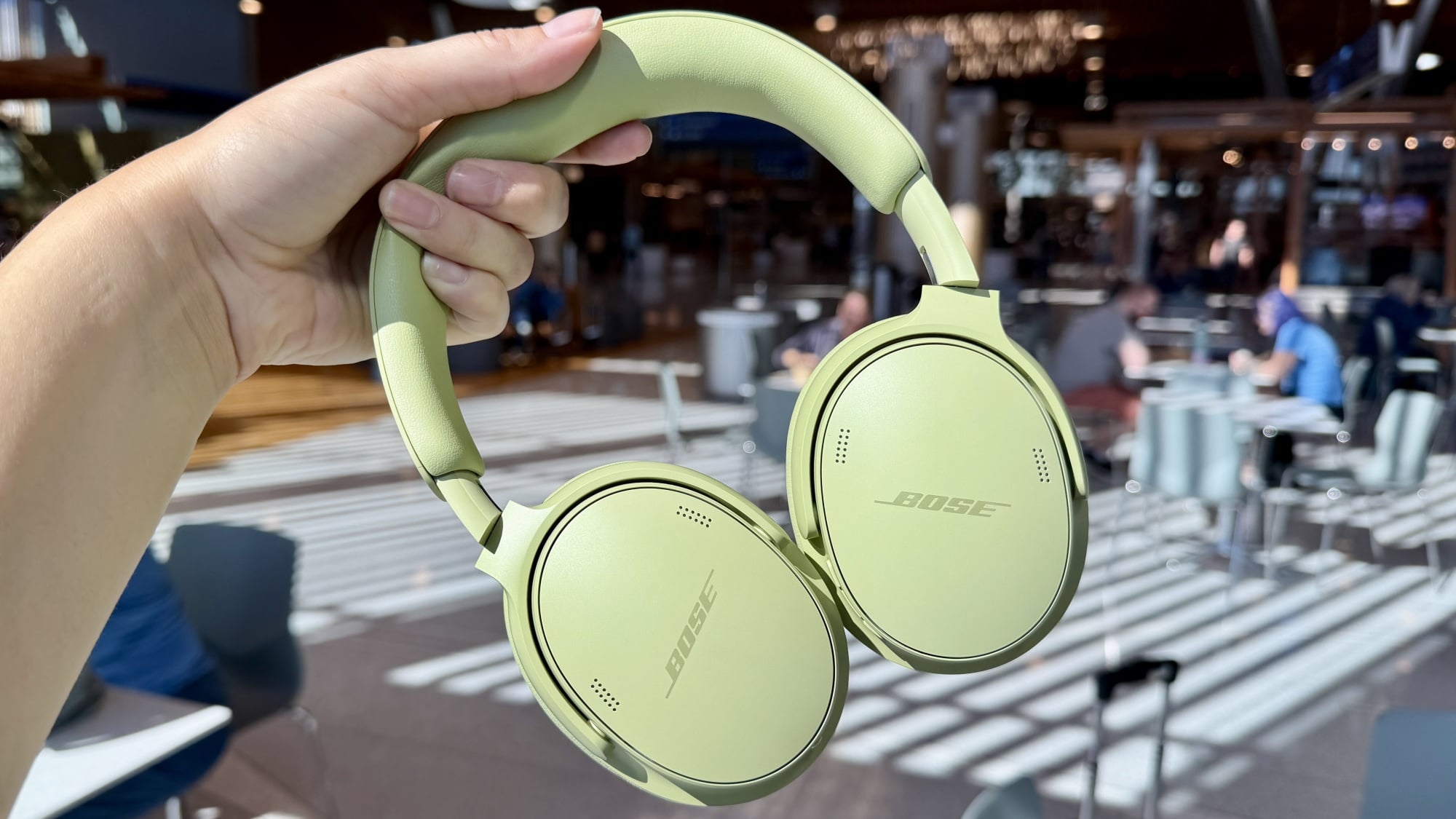 person holding green bose headphones in front of airport terminal