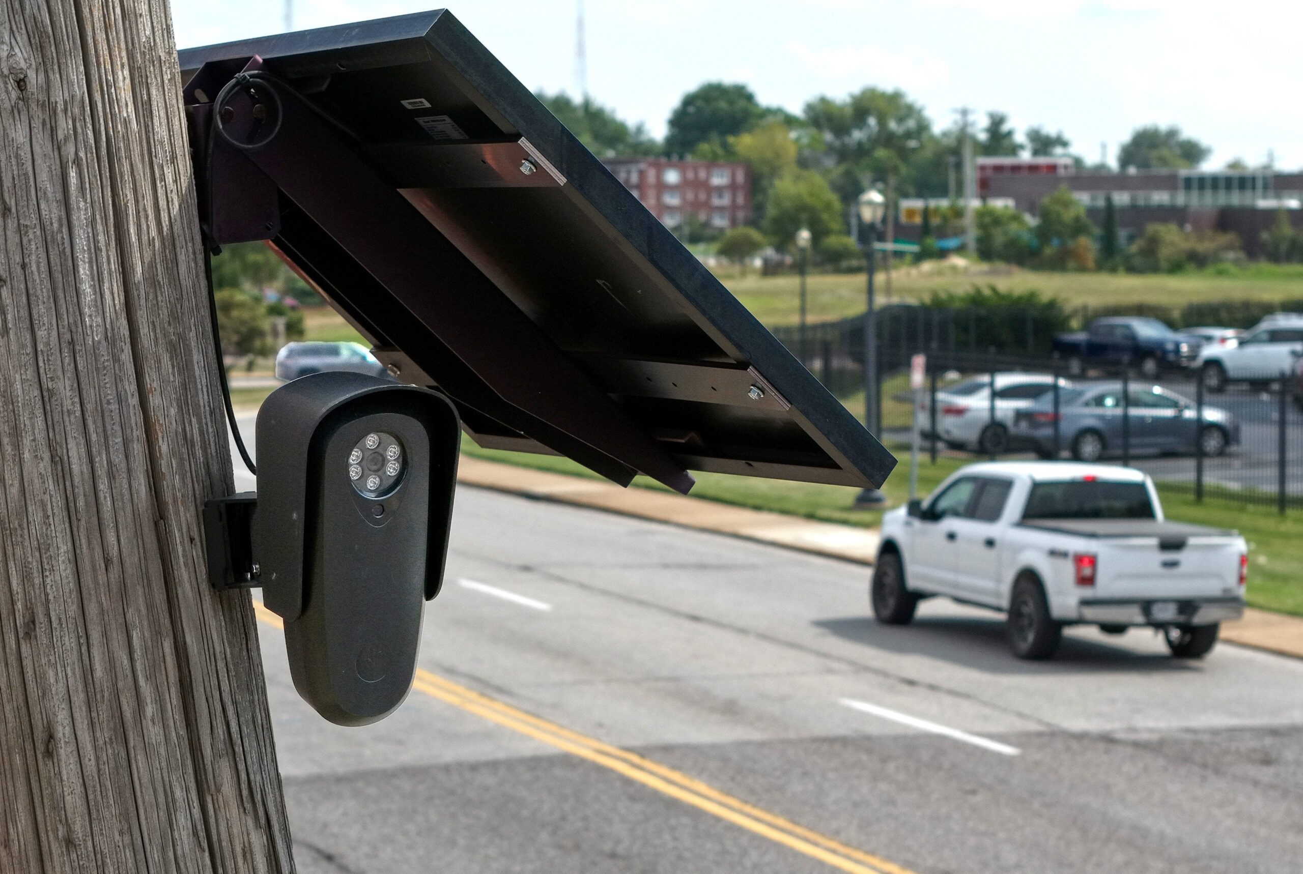 A Flock camera on a tall light post. A truck drives by underneath.