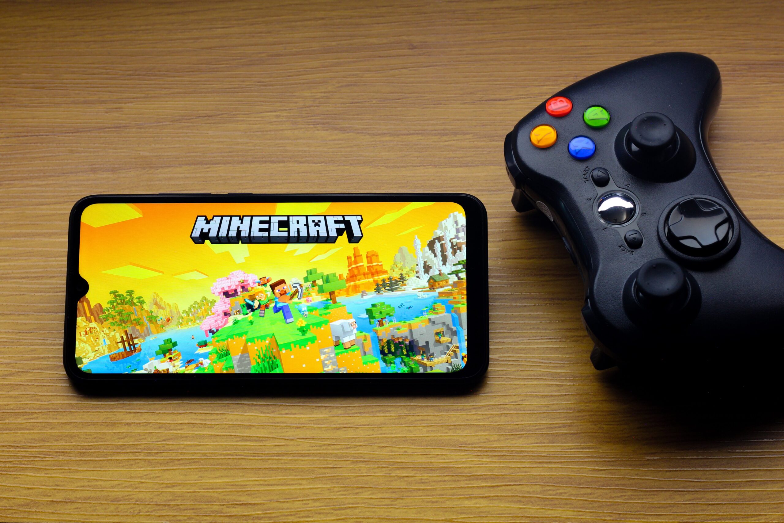 the Minecraft logo is seen displayed on a smartphone screen next to an Xbox video game controller.