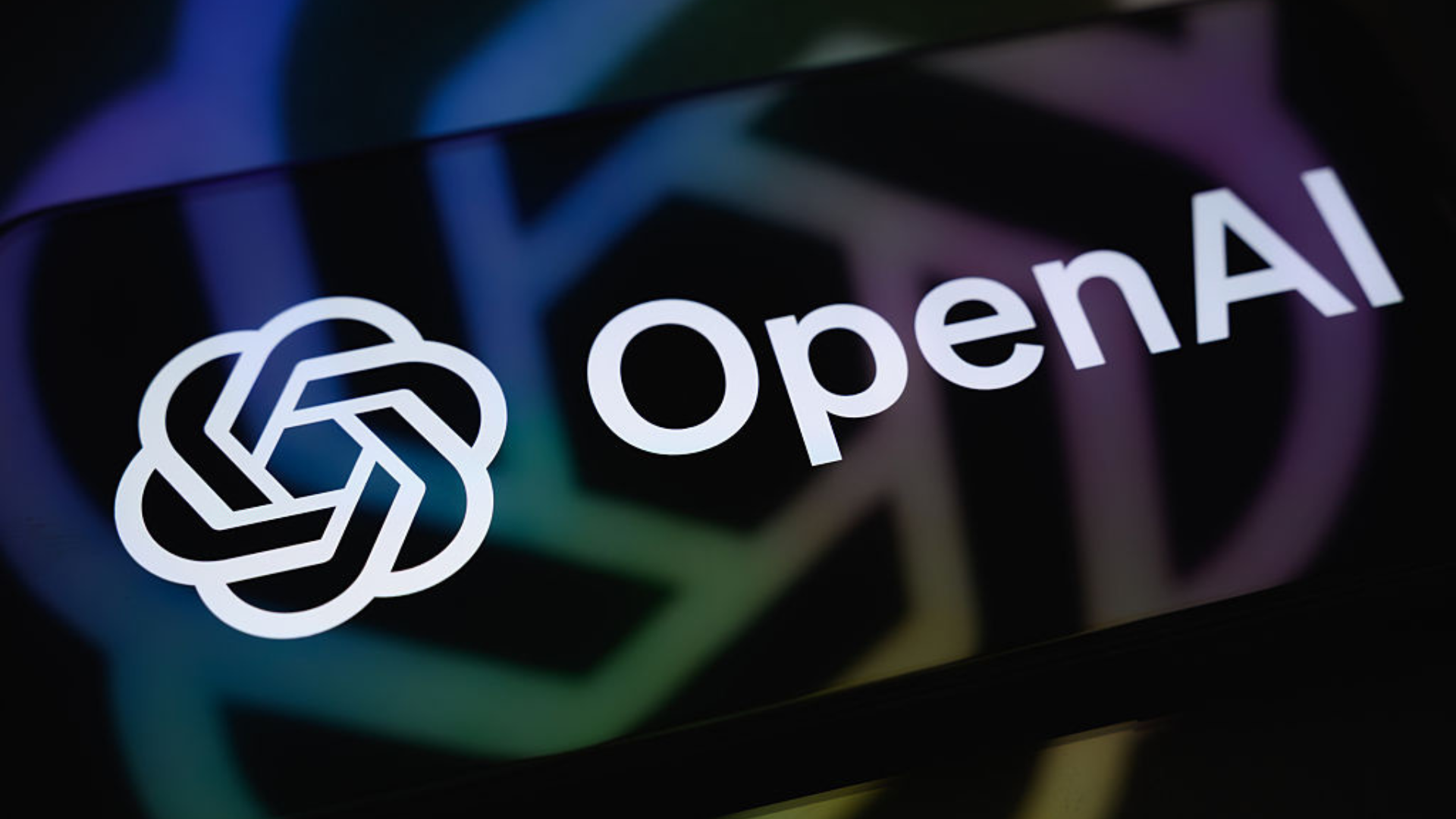 The OpenAI logo is displayed on a smartphone screen resting on a reflective surface with the company's logo projected onto it.